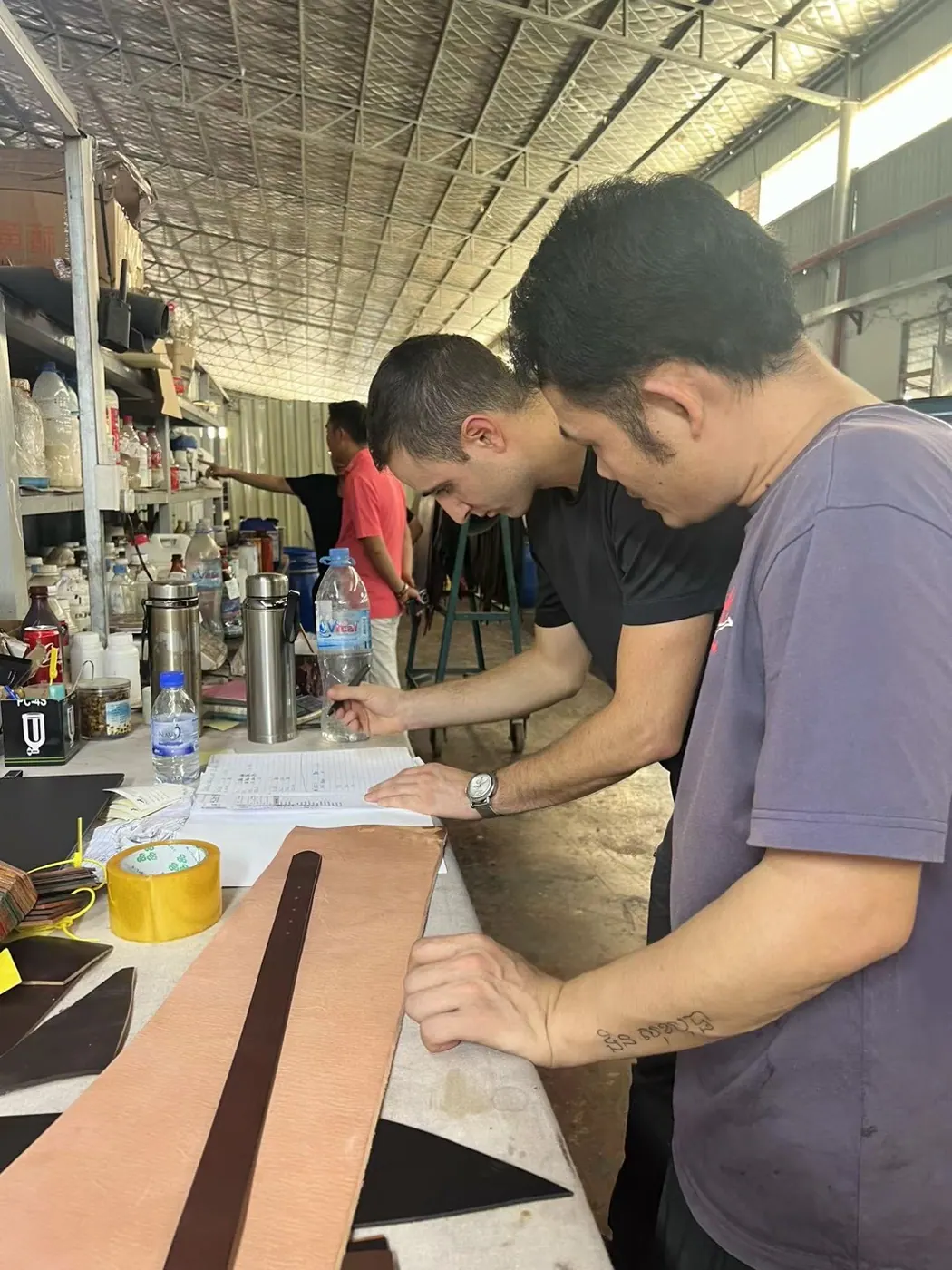 workers measuring and marking leather belt straps by hand in a belt factory