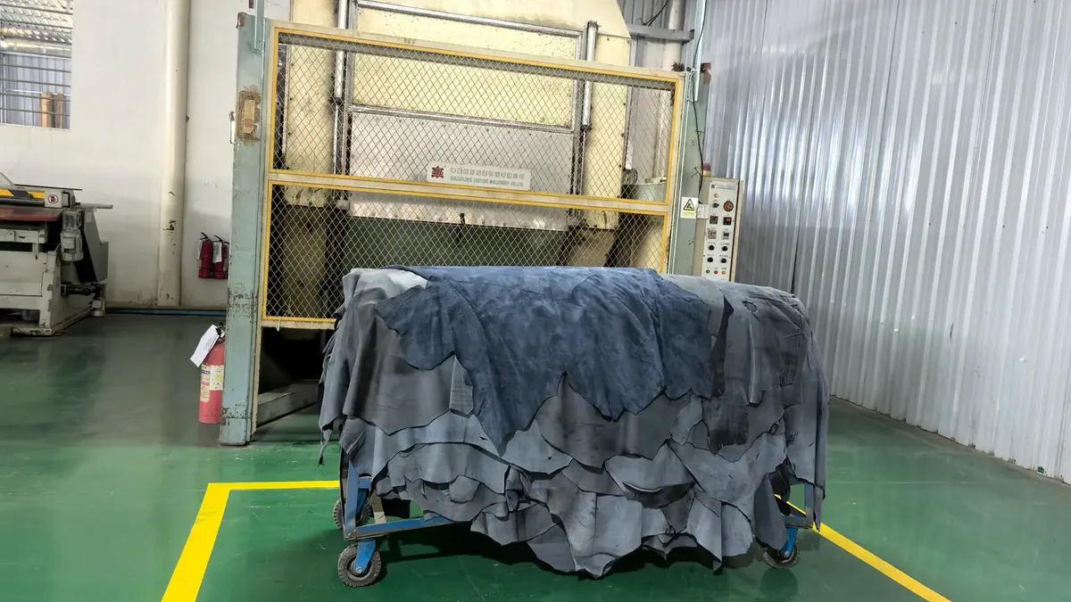 Processed leather hides staged on a trolley beside finishing equipment