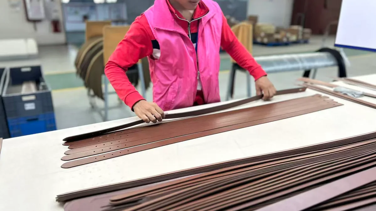 Worker aligning cut brown belt straps at a factory workstation